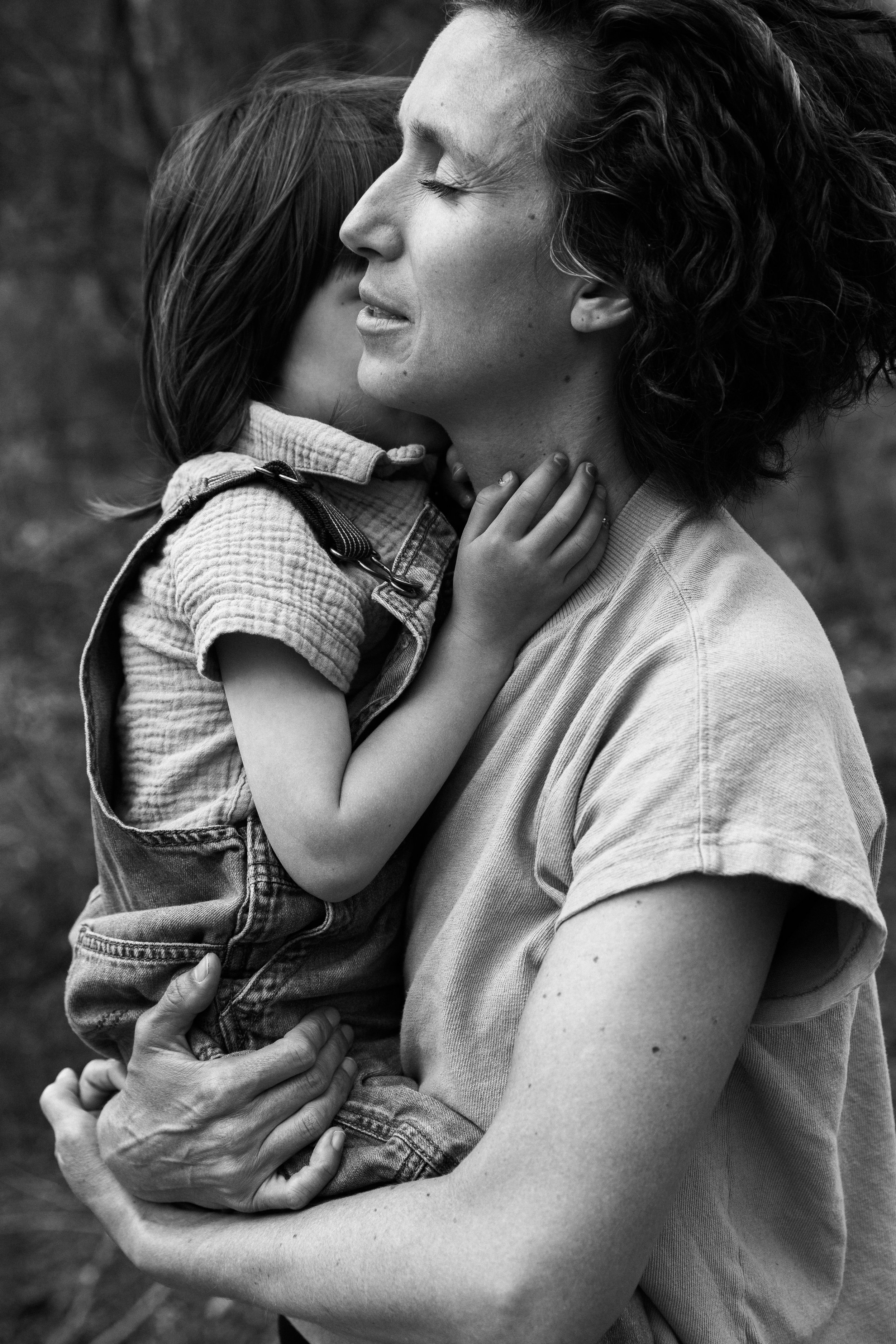 Black and white photo of a woman hugging a young girl tightly, both with their eyes closed, conveying a sense of comfort and affection.