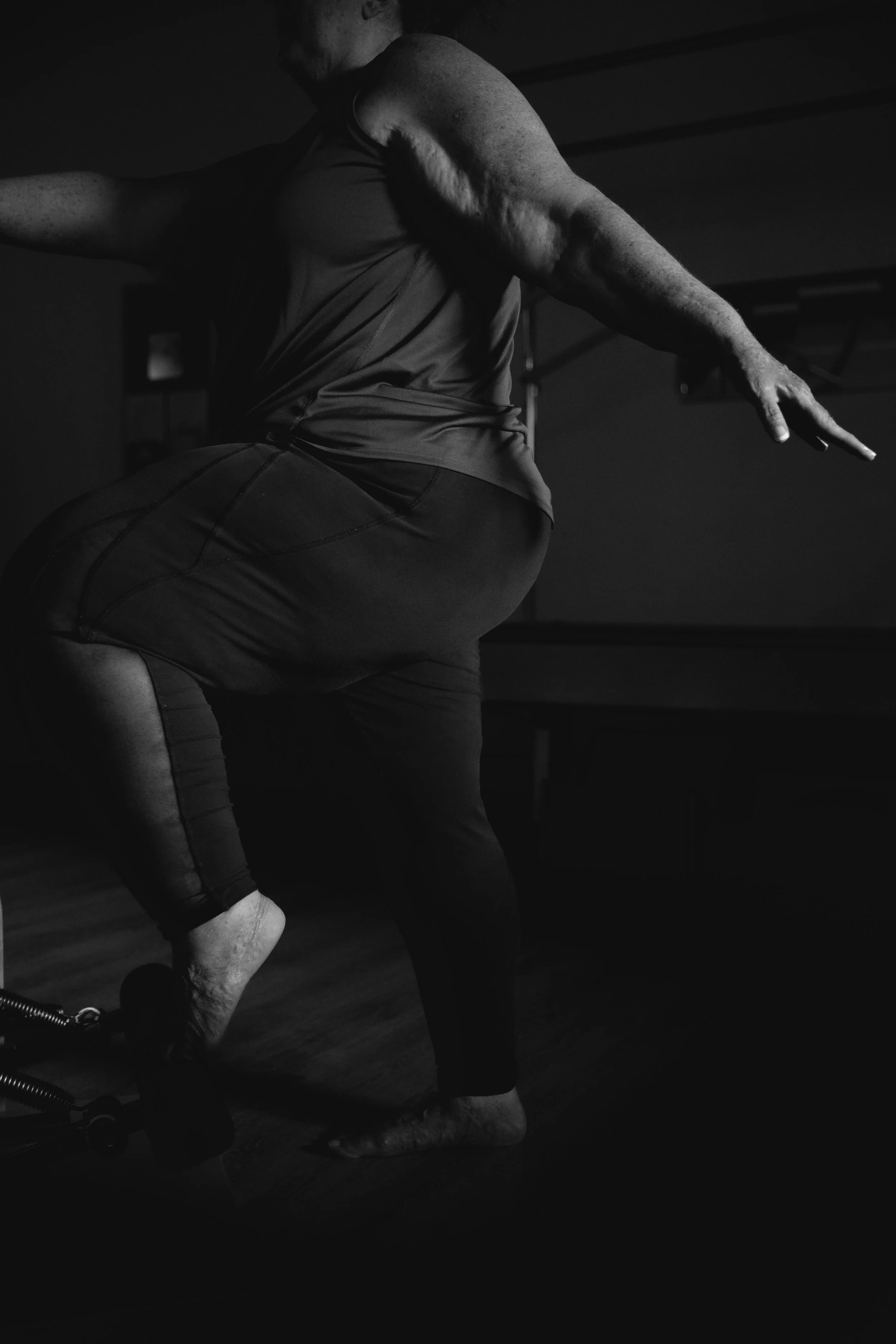 A person practicing yoga or stretching, kneeling on the floor with arms extended and one foot behind them, in a dimly lit room.