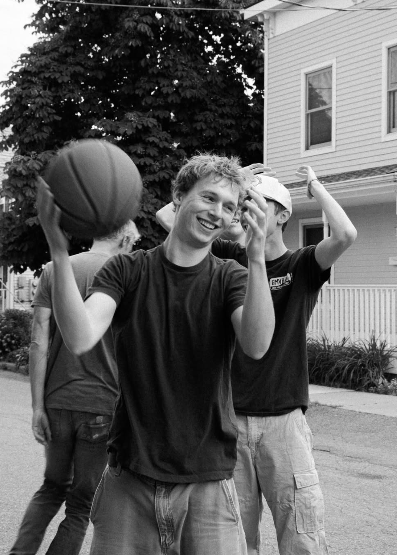 Young man smiling and holding a basketball outdoors in a residential neighborhood.
