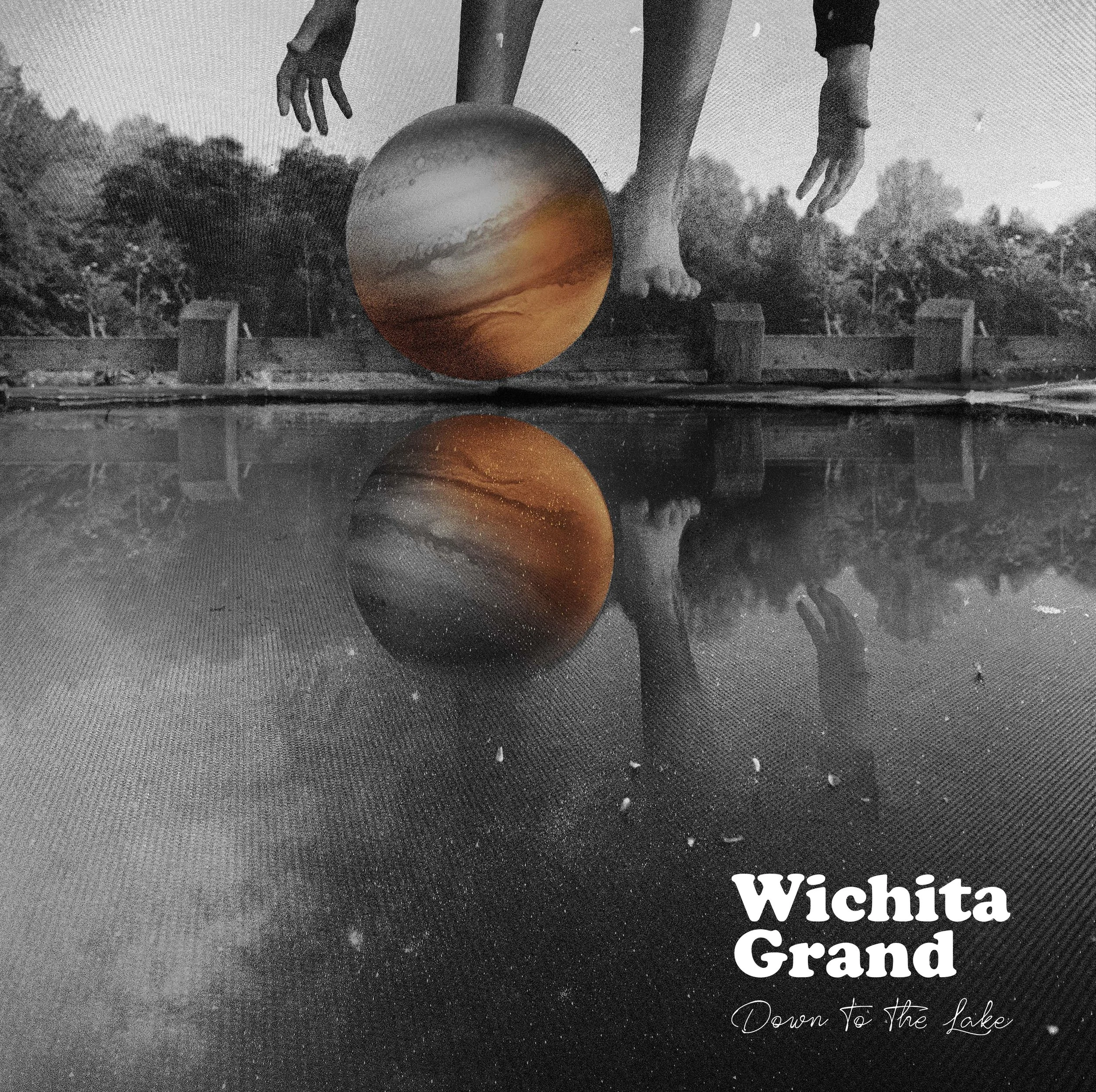 Black and white photograph of a person reaching down to touch the water at a lake or river. There is an orange sunset or sunrise reflected in the water. Text on the bottom right corner reads 'Wichita Grand' and 'Down to the lake.'