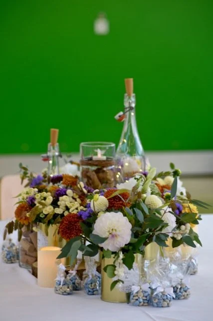 Centre de table floral avec bougies, bouteilles en verre, et décoration pour célébration, sur une table