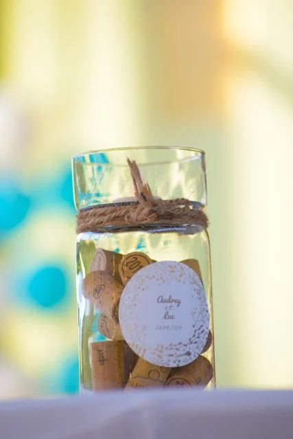 Un verre en verre rempli de pièces de monnaie, avec un ruban en cordeau autour du haut, sur un fond flou aux couleurs pastel.