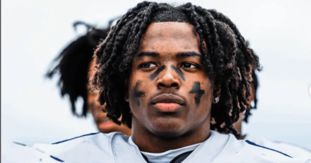 Close-up of a young football player with face paint, wearing a white jersey, and dreadlocked hair.