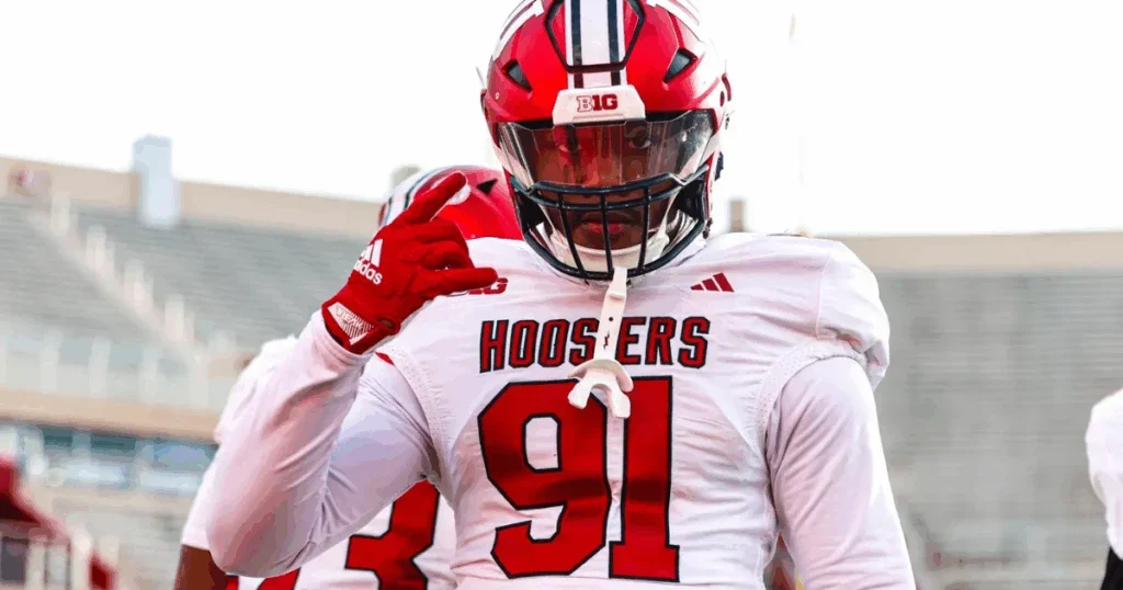 A football player in a white and red uniform and helmet making a gesture on the field.