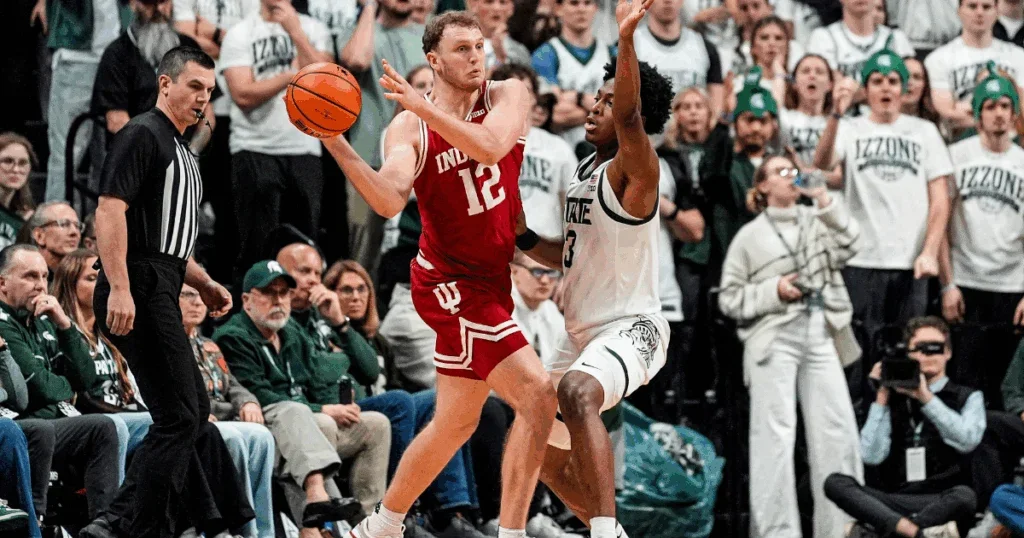 Two basketball players are competing during a game, with a crowd of spectators watching.