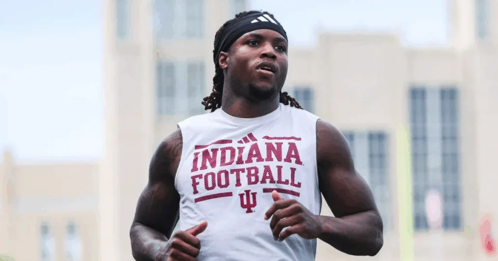 A young man running outdoors wearing a sleeveless Indiana football shirt and a black headband.