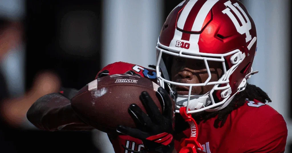 A football player in a red helmet and jersey catching a football during a game.