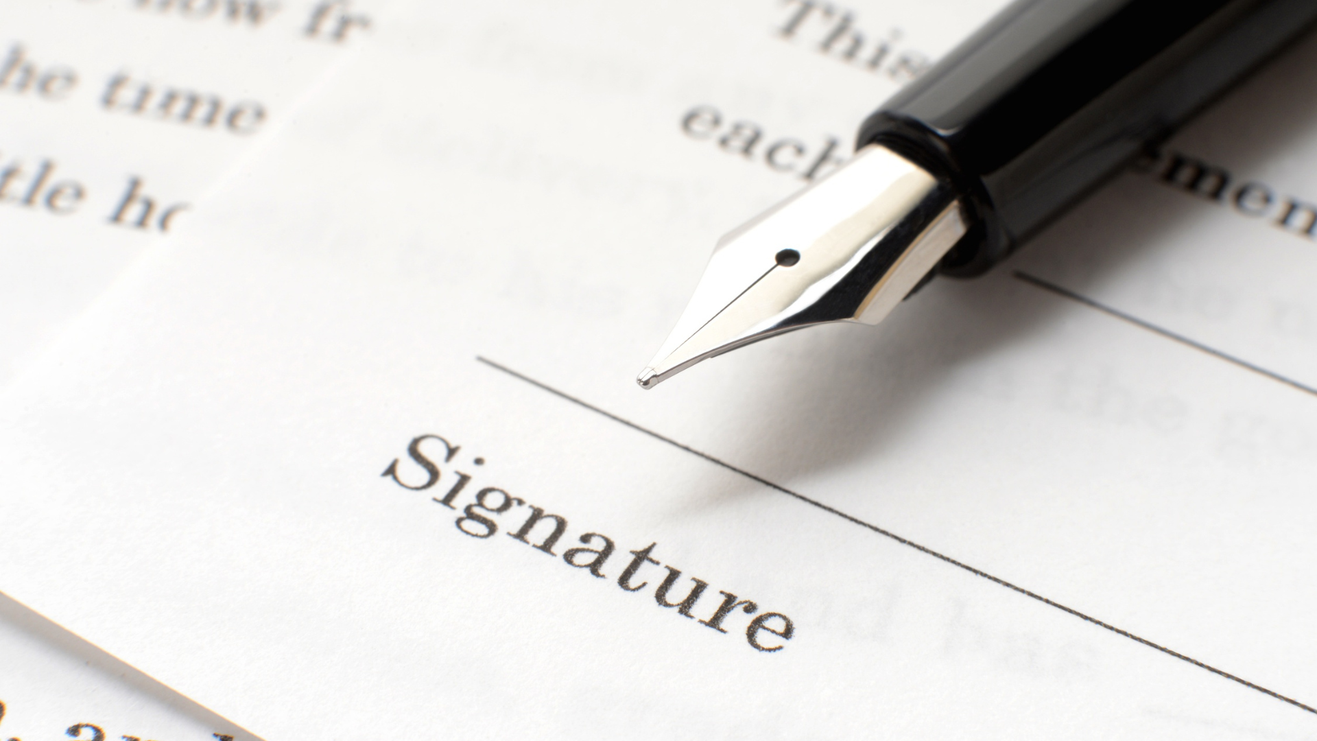 Close-up of a black fountain pen writing a signature on a document with the word "Signature" visible.