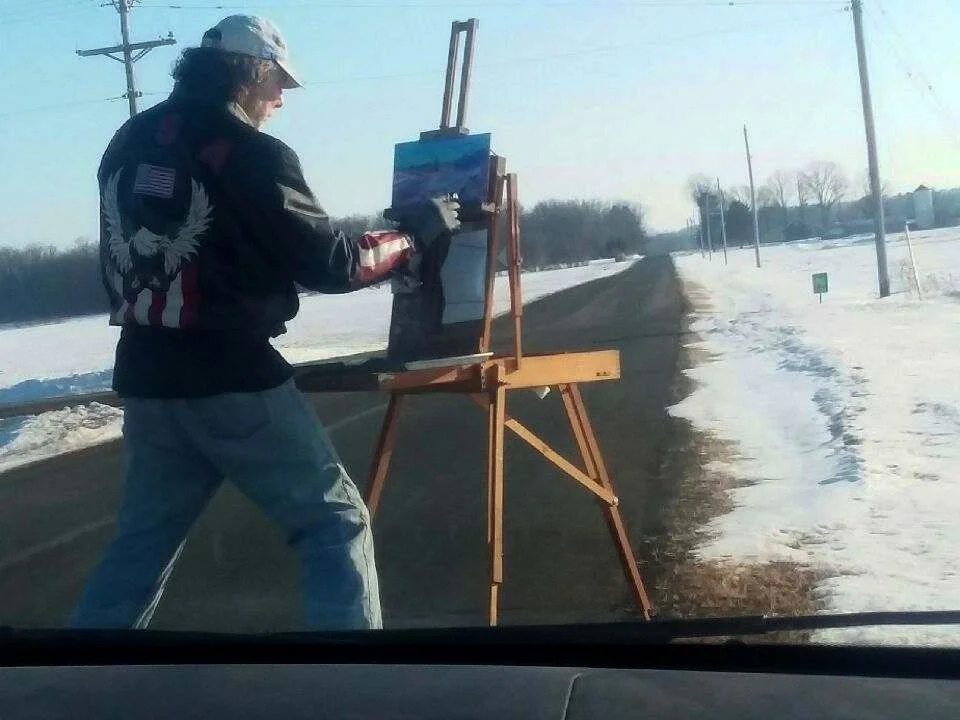 Person painting on outdoor easel beside a rural road in winter.