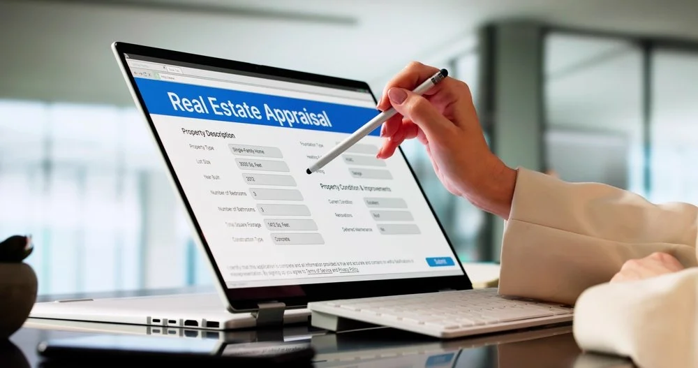 Person filling out a real estate appraisal form on a laptop screen with a stylus in a bright, modern office.