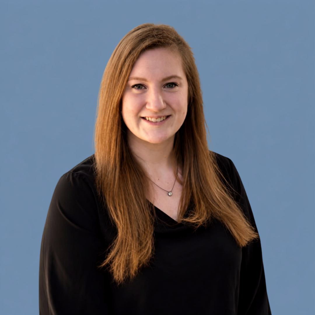 A young woman with long, reddish-brown hair, wearing a black top and a necklace, smiling against a solid blue background.
