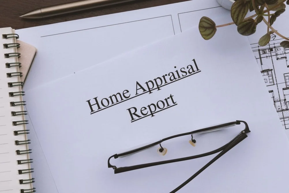 A report titled Home Appraisal Report on a table, with a pair of glasses, a pen, and architectural plans nearby.