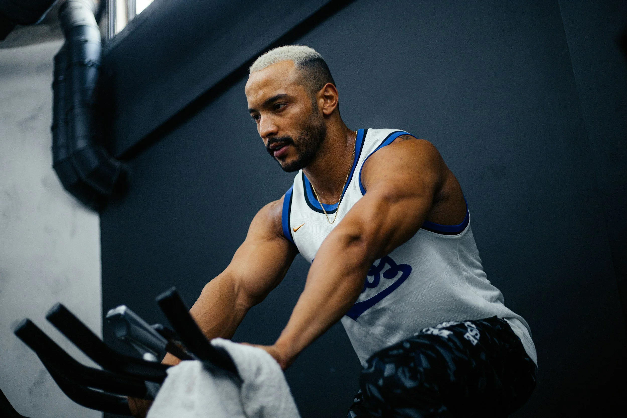 Man with blonde hair working out on exercise bike in gym.