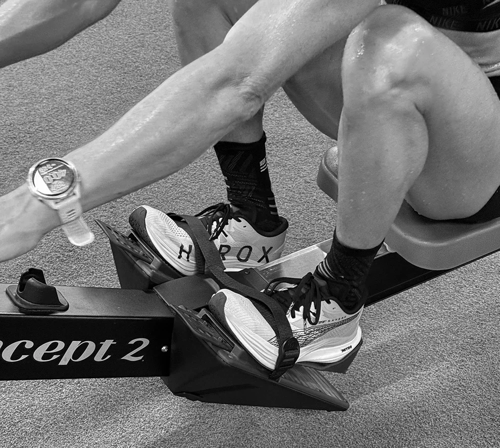 Closeup of a woman on a rowing machine showing shoes, hands, and a watch