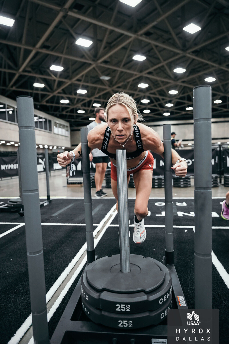 A woman in athletic gear pushing a weighted sled at an indoor gym during a workout session.