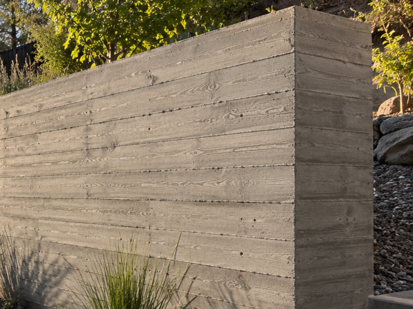 A large wooden retaining wall made of horizontal planks with visible wood grain, situated outdoors with greenery and rocks in the background.