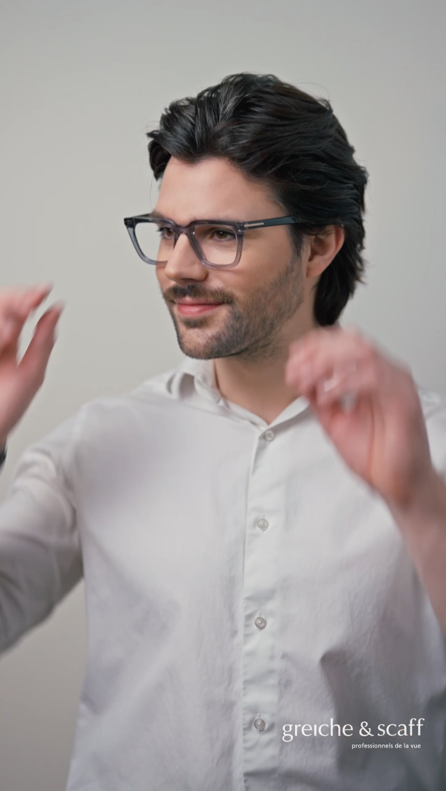 Production vidéo pour Greiche & Scaff. Un homme portant des lunettes et une chemise blanche sourit, semble ajuster ou porter ses lunettes. Fond neutre, texte en bas à droite : 'greiche & scaff, professionnels de la vue'.