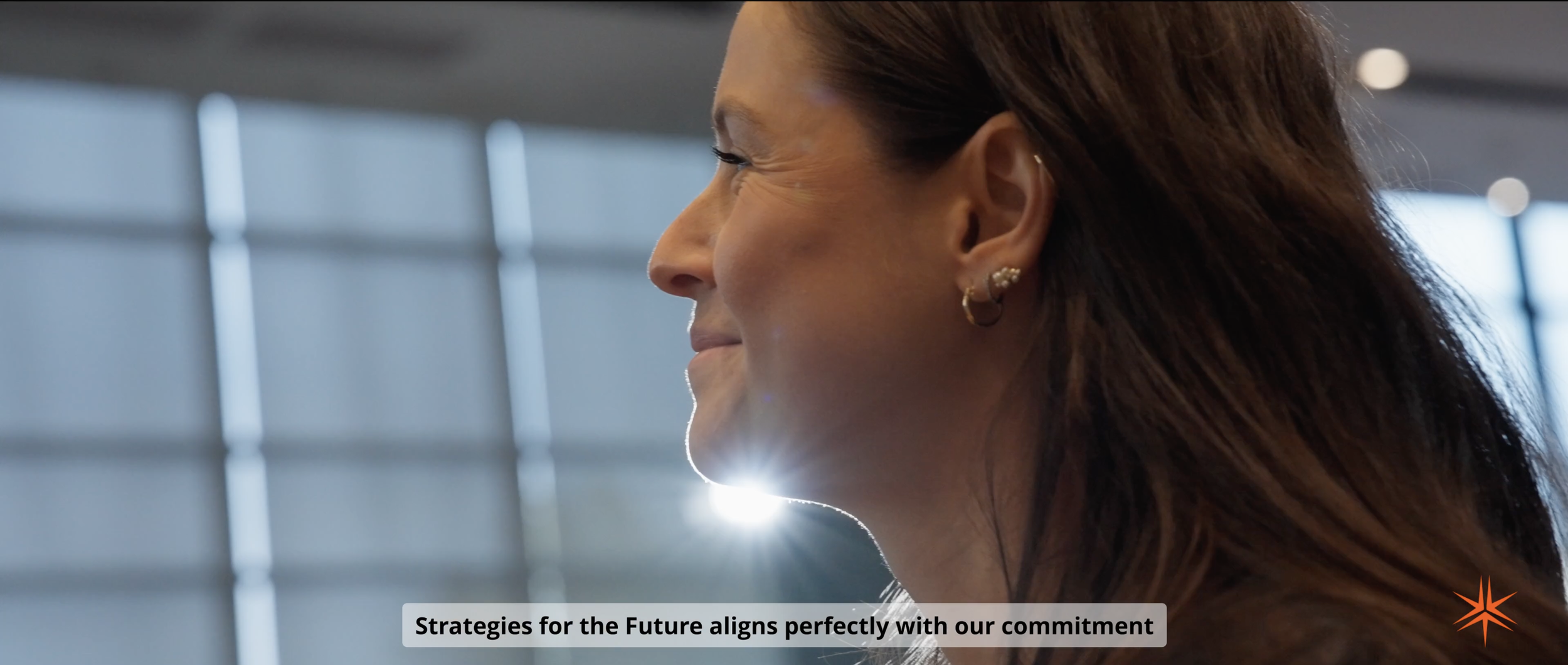 Profil d'une femme avec des boucles d'oreilles, souriant, dans un environnement moderne avec une lumière brillante en arrière-plan.