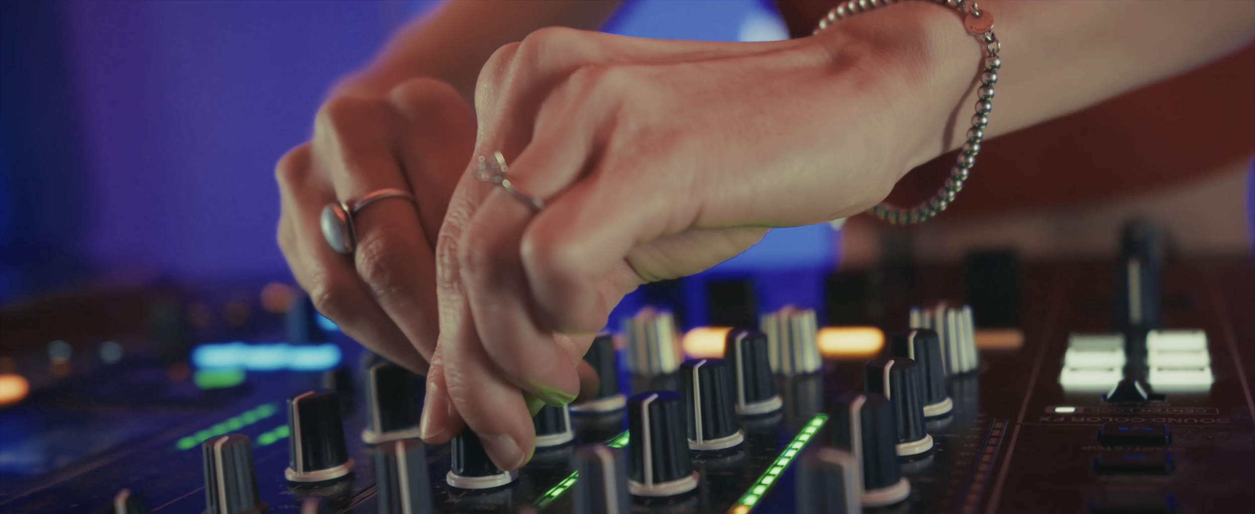 Main manipulant un contrôleur DJ avec des boutons, des curseurs et des lumières LED colorées dans un environnement sombre.