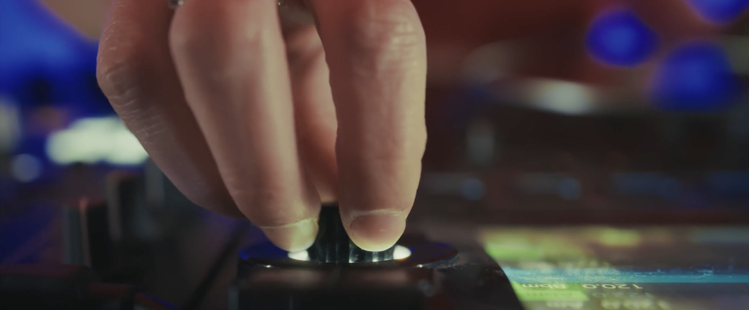 Une main ajuste un bouton sur une platine de DJ, avec un écran lumineux en arrière-plan.