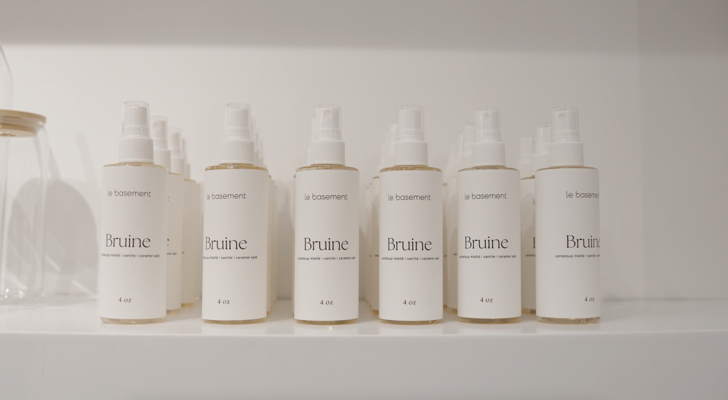 Une rangée de bouteilles blanches de spray nommées 'Bruine' avec des étiquettes indiquant 'le basement', '4 oz' et des saveurs comme 'vanille' et 'caramel salé'.