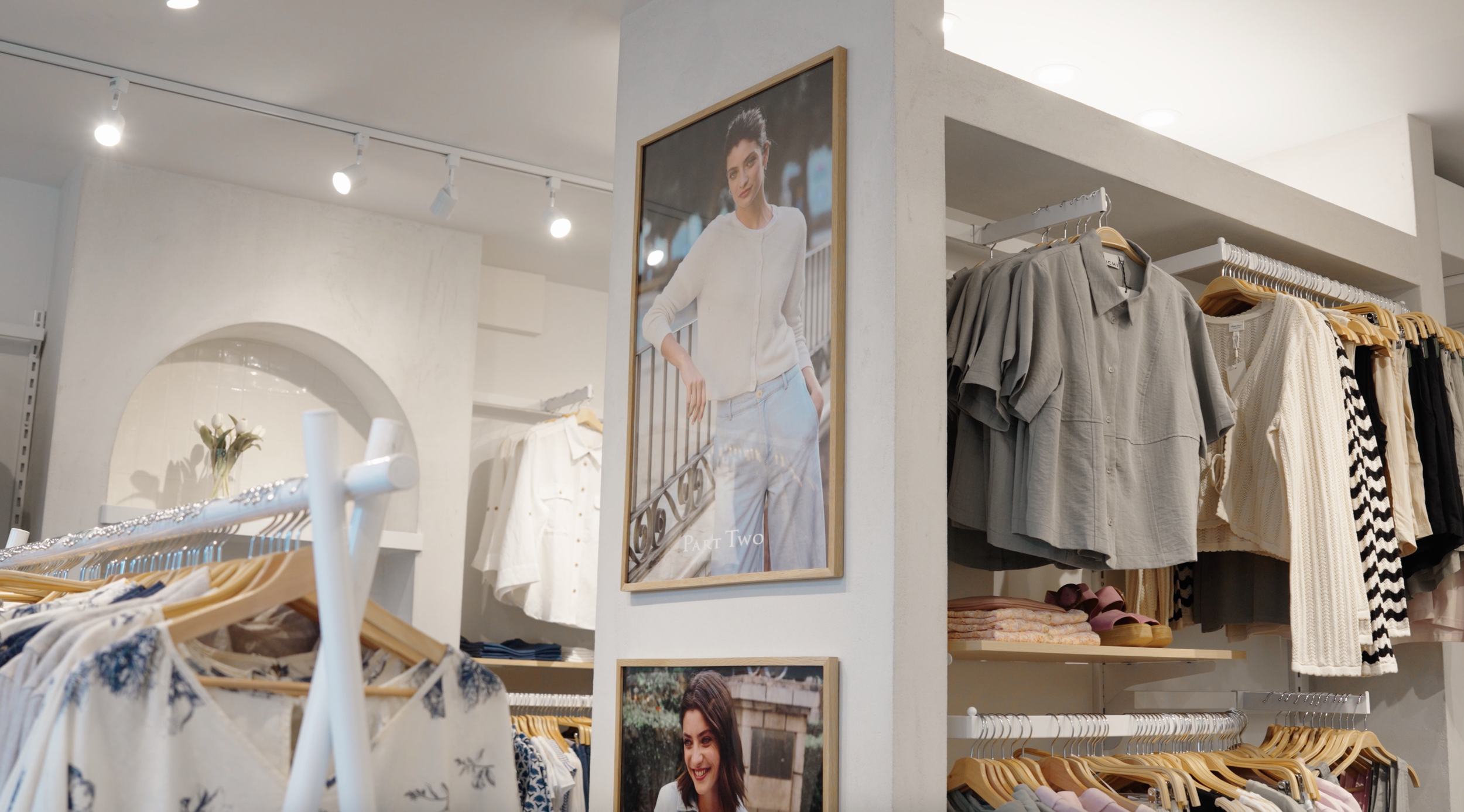 Vue intérieure d'un magasin de vêtements avec des vêtements suspendus et des affiches de mode sur le mur.
