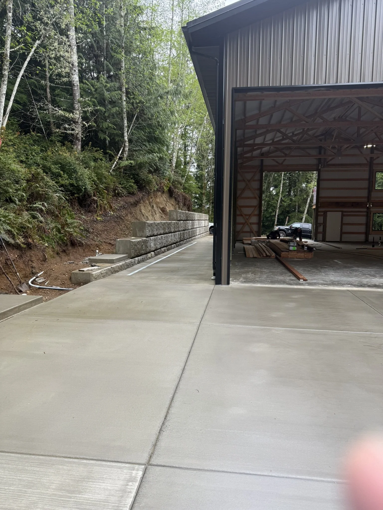 Finished poured concrete driveway and large metal garage shop building with a retaining wall 