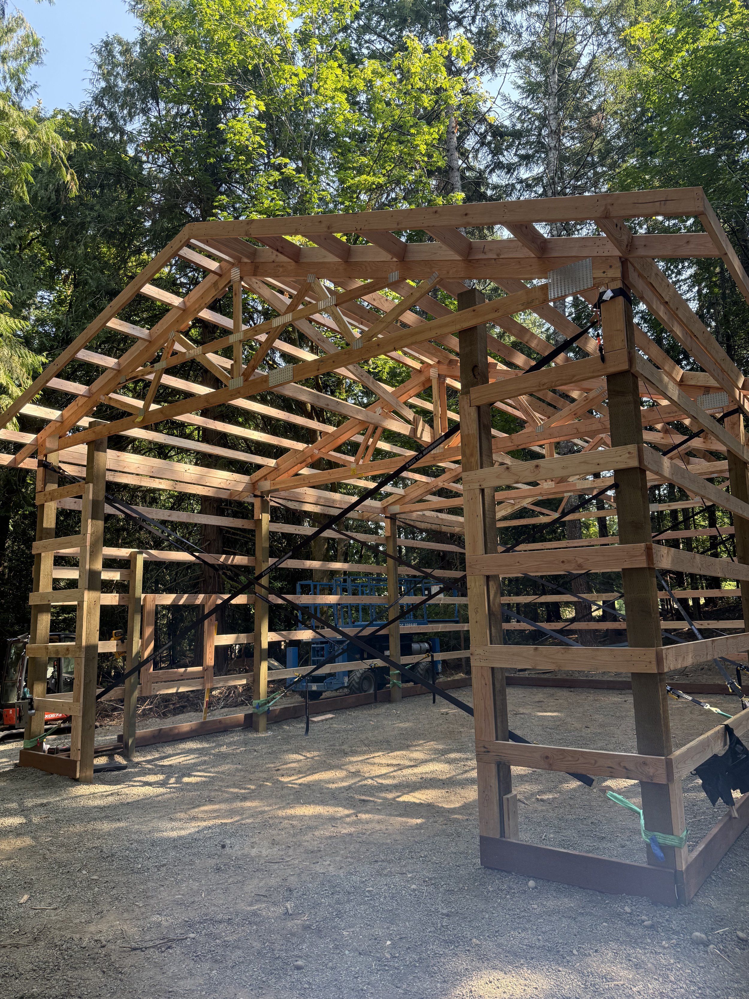 Wooden framing structure under construction in a wooded area with trees in the background.