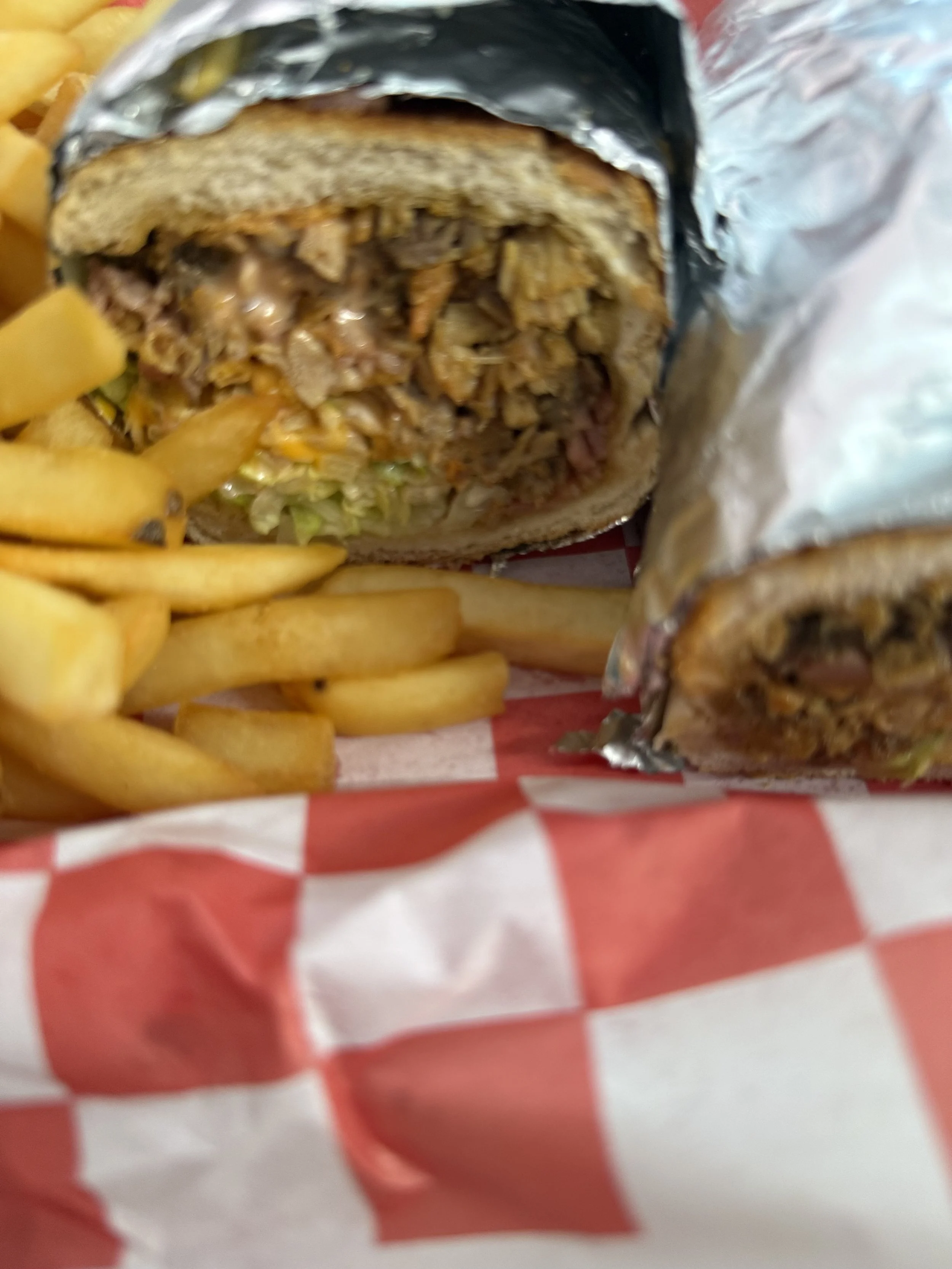 Close-up of a burrito with shredded meat, rice, and vegetables, partially wrapped in foil, alongside a serving of French fries in a red and white checkered paper.