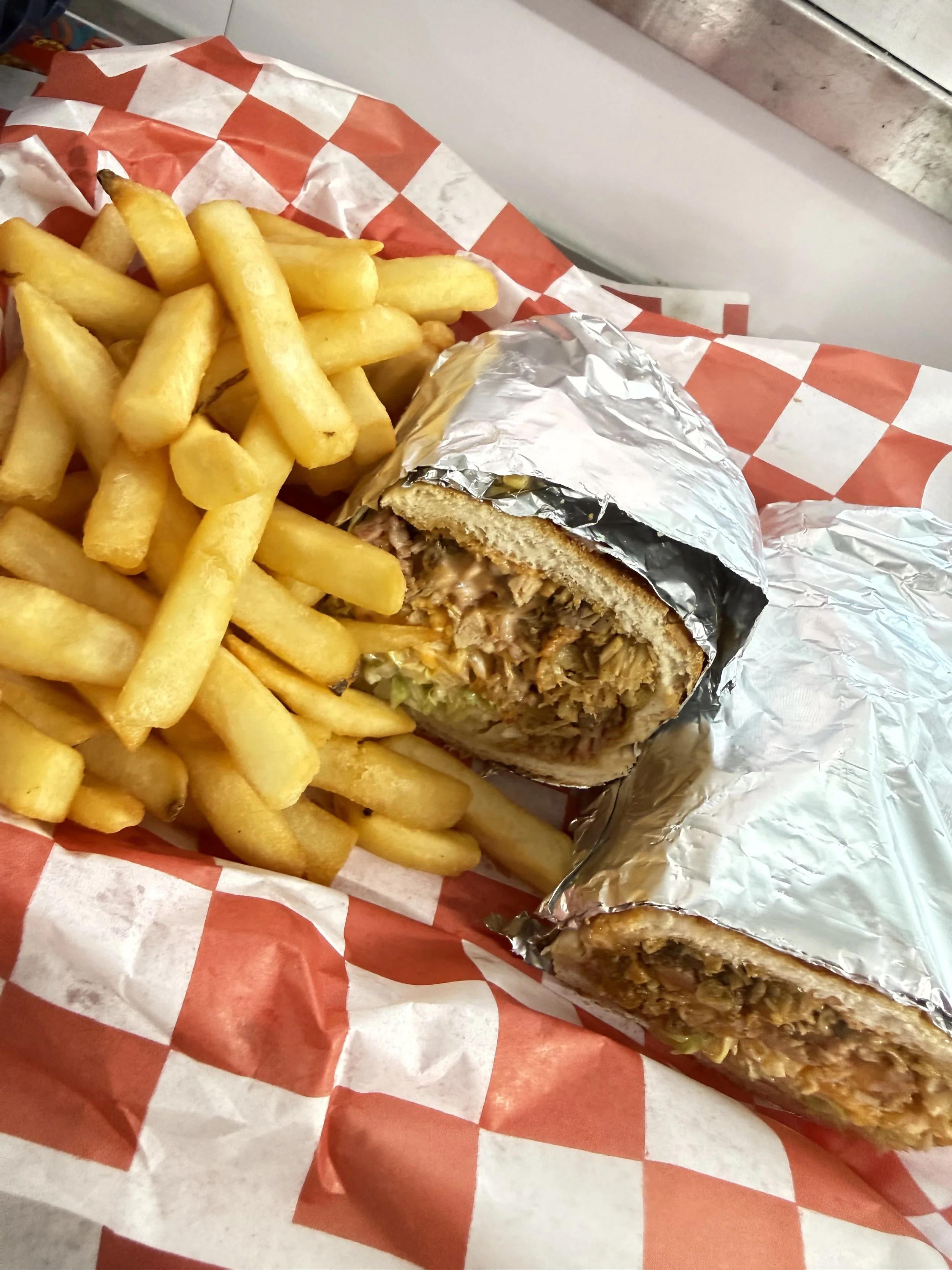 French fries and a partially unwrapped burrito wrapped in foil, on a red and white checkered paper.