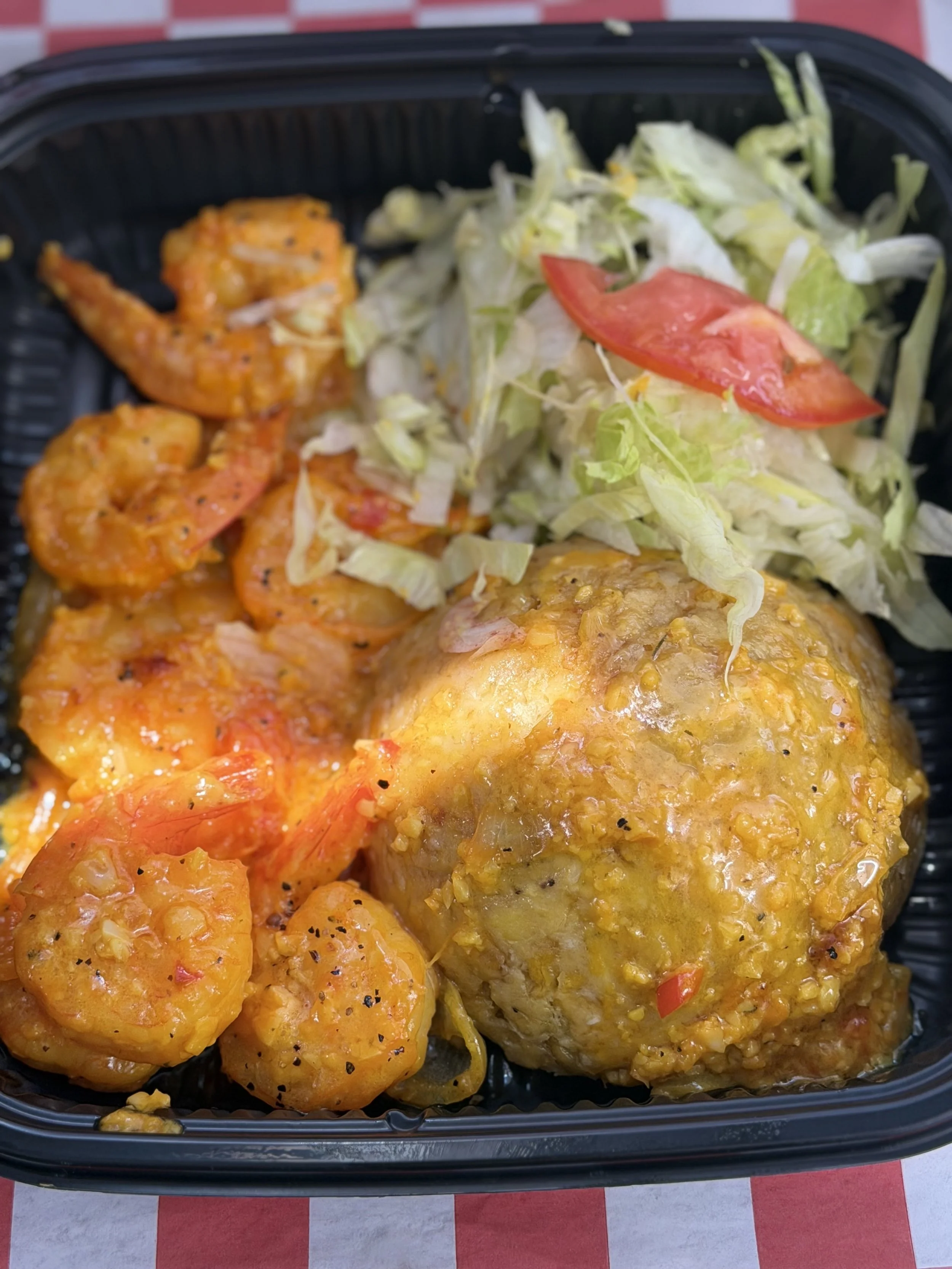 A takeout container with shrimp, seasoned chicken breast, and a side salad with lettuce and tomato slices.