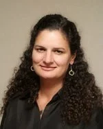 A woman with curly dark hair wearing a black top and earrings, smiling at the camera.