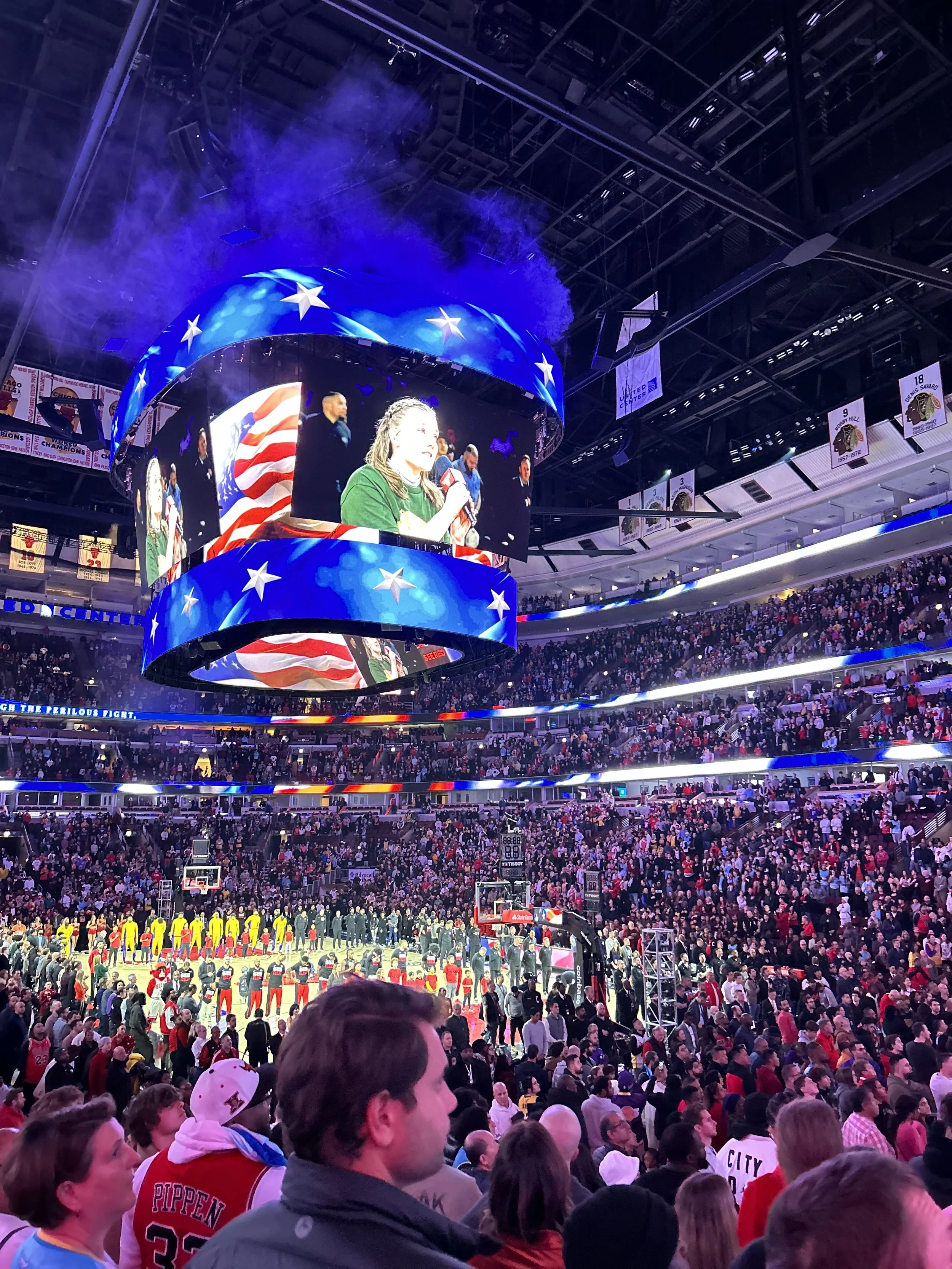 Meredith a person on long hair holding a microphone on the Jumbotron at a packed Chicago Bulls game.