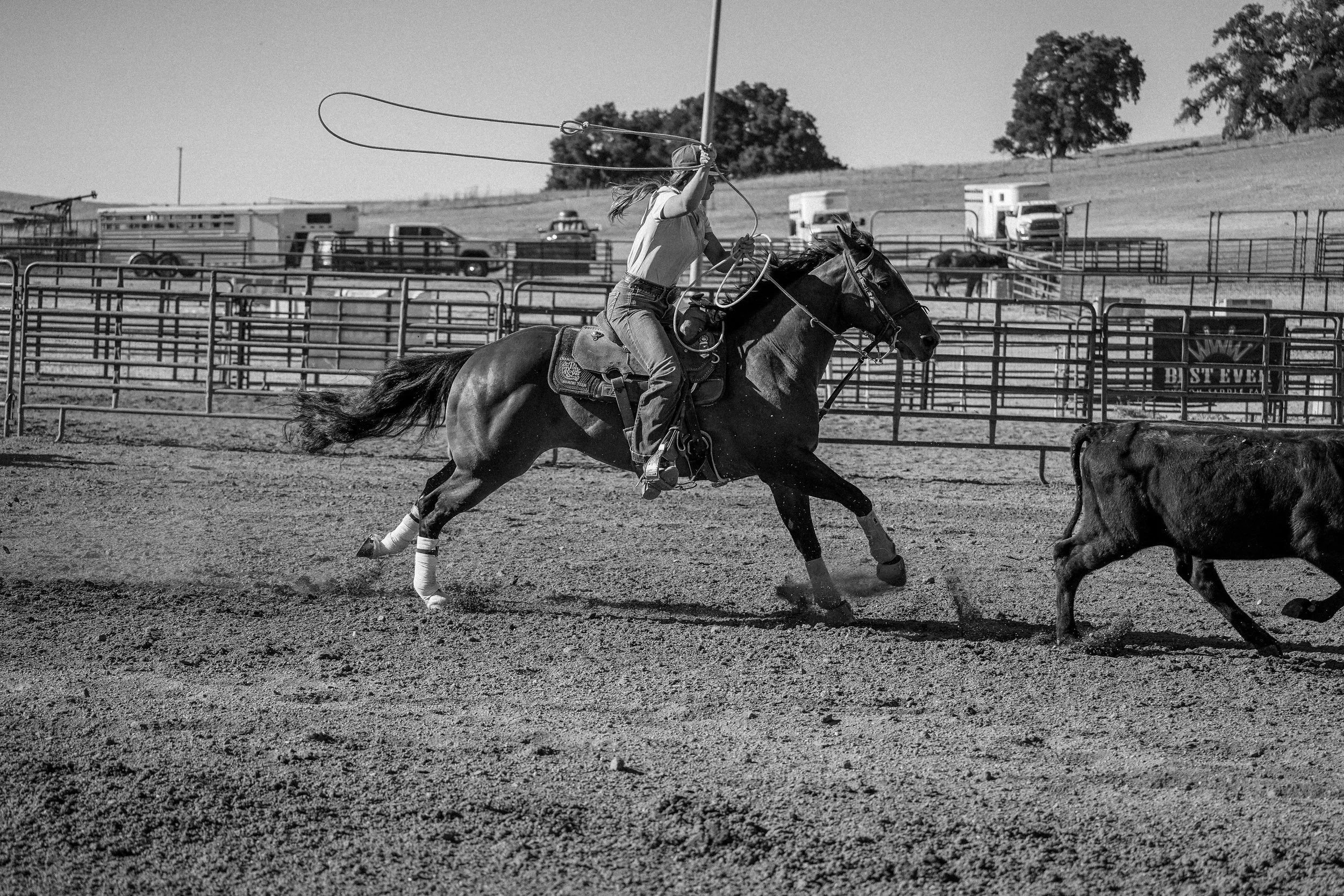 A woman riding a horse and waving a lasso in an outdoor arena