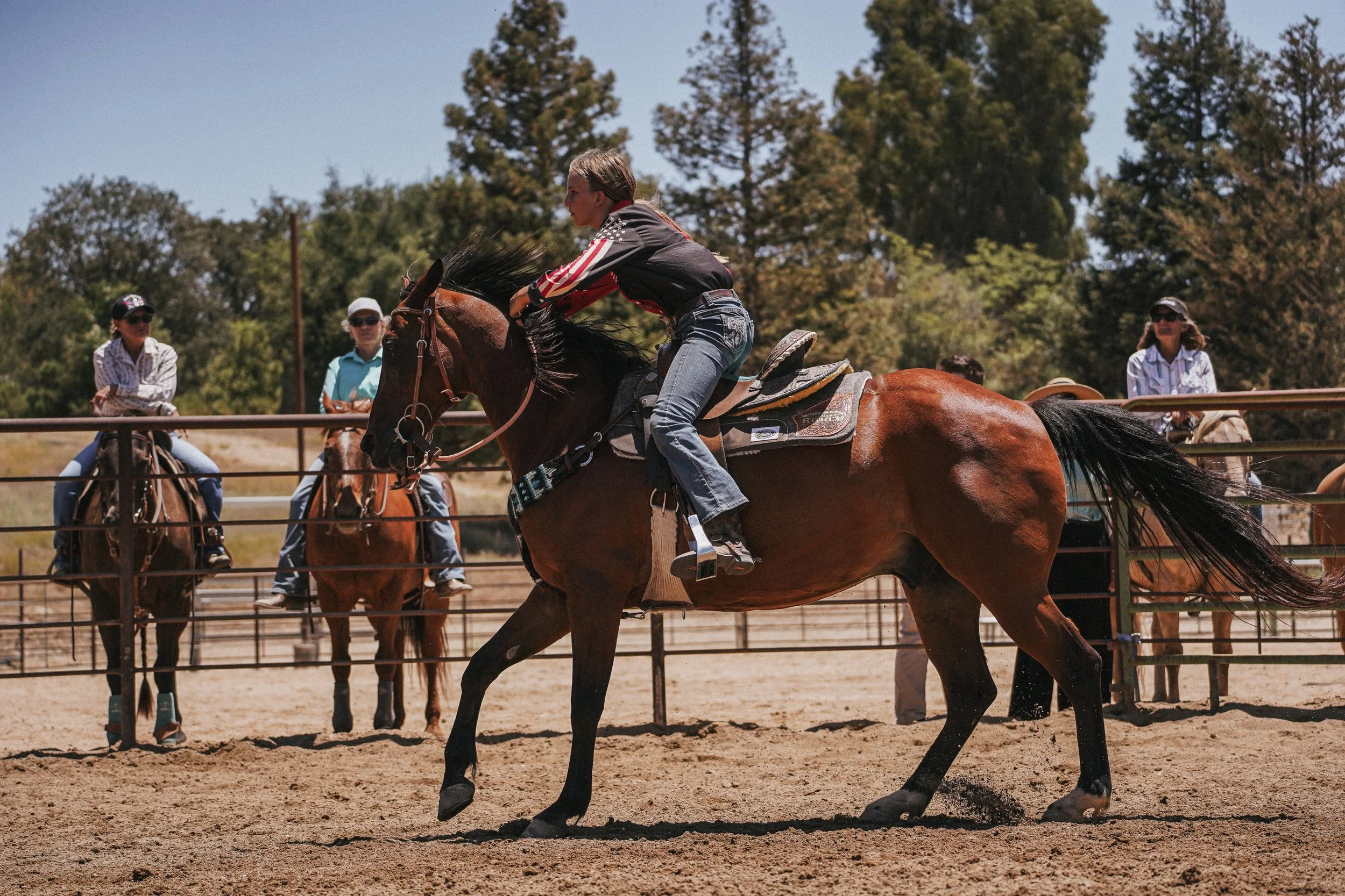 A woman riding a horse during a rodeo or horseback riding event, with several other riders and spectators watching in the background.