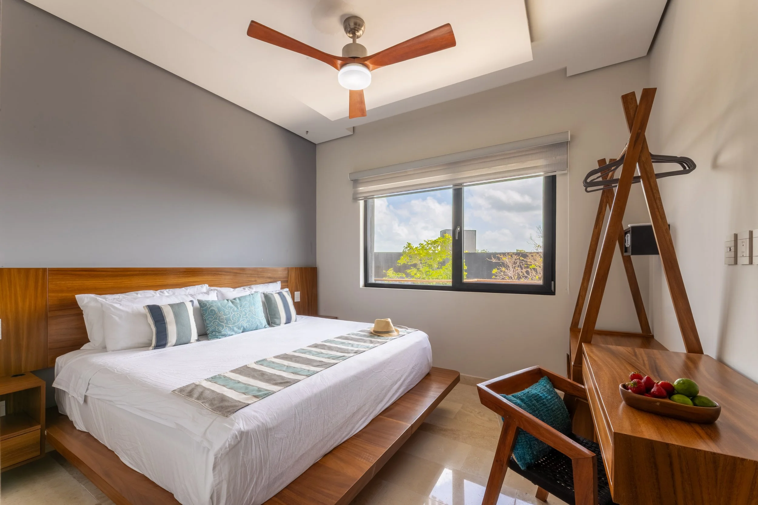 Real estate photography of a modern bedroom with a large bed, wooden headboard, and pillows, at Amira Tulum.