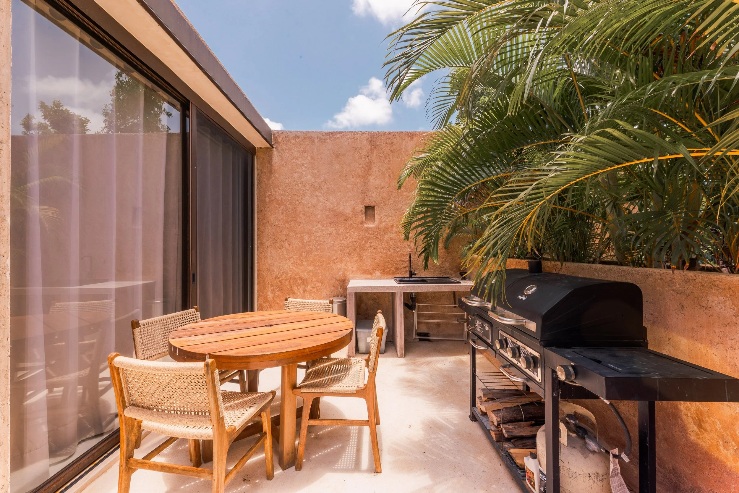 Real estate photography of an outdoor patio area with a round wooden table and four wicker chairs, at Tulum.