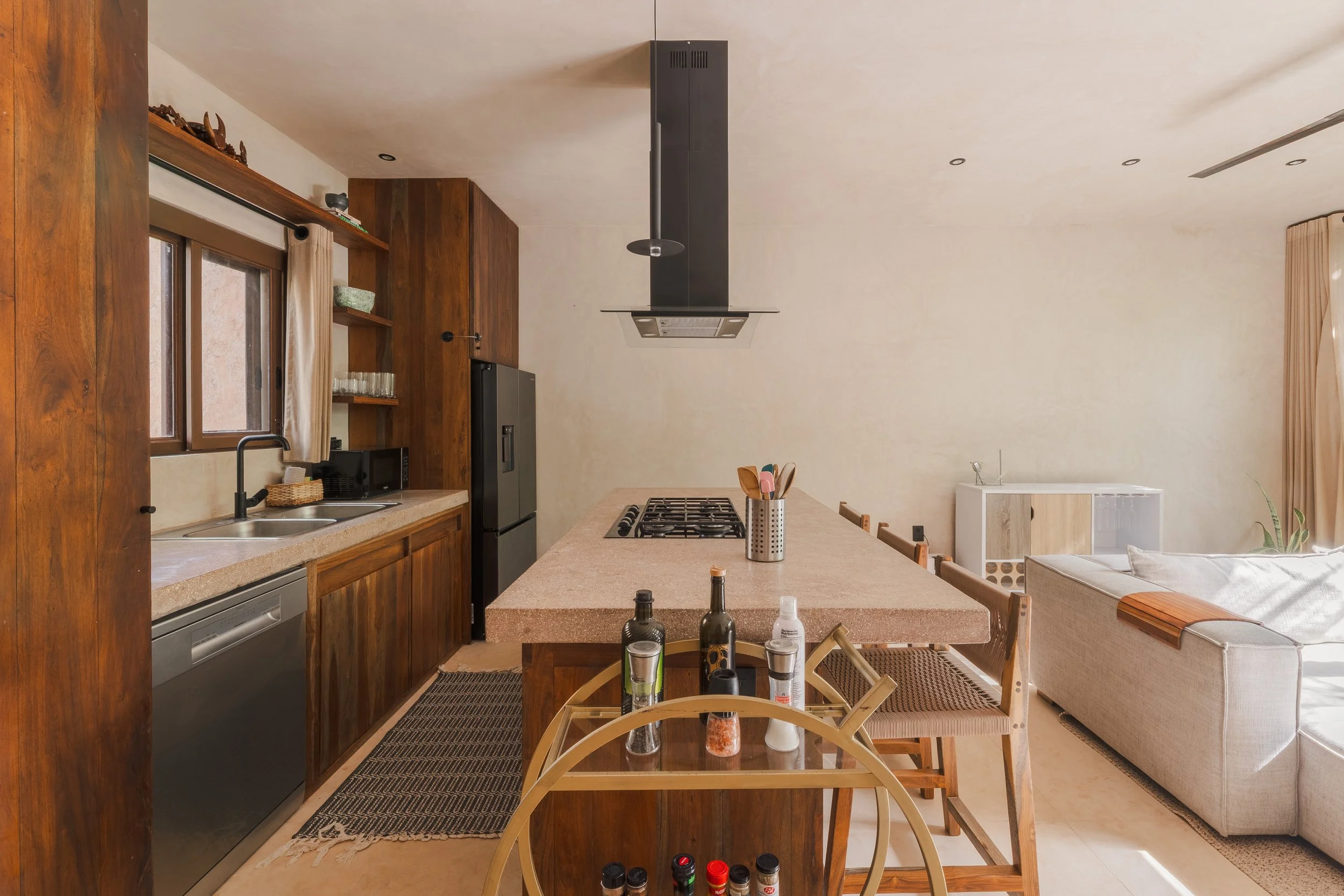 Real estate photography of a modern kitchen with wooden cabinets, stainless steel appliances, a beige countertop, and a gas stove, at Tulum.