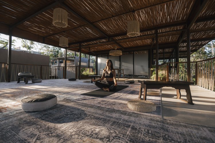 Woman practicing yoga in a spacious, open-air studio with wooden ceiling and natural lighting, at Siwa Tulum.