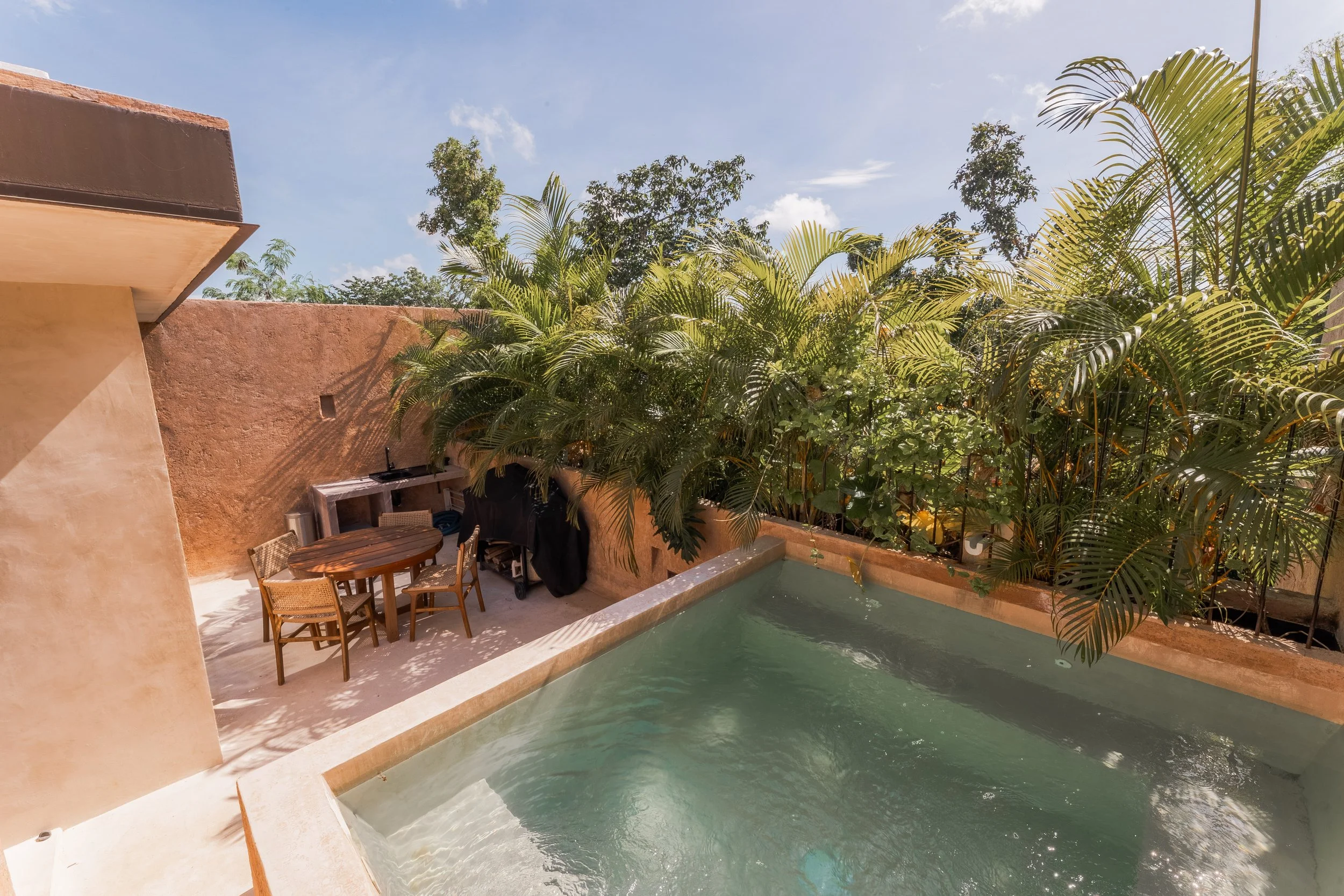 Real estate photography of a backyard patio with a small pool, surrounded by a tan stucco wall and lush green palm trees at Tulum.