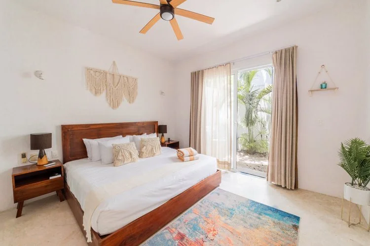 Real estate photography of a bedroom with a wooden bed frame, white bedding, and beige pillows, at Tulum
