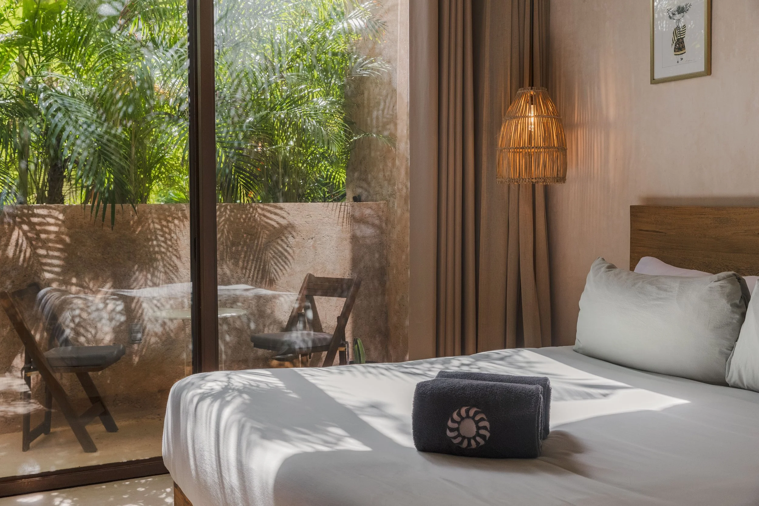 Real estate photography of a view of a bedroom with a large glass window showing green plants outside, at Tulum.