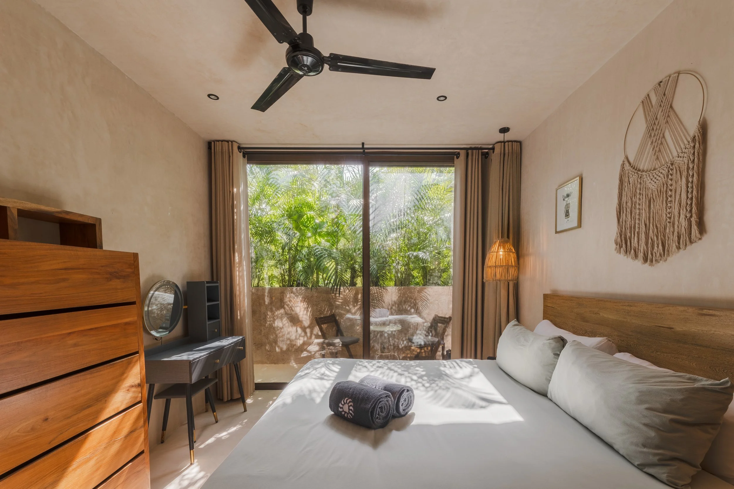 Real estate photography of a bedroom with a large window showing lush green plants outside, at Tulum.