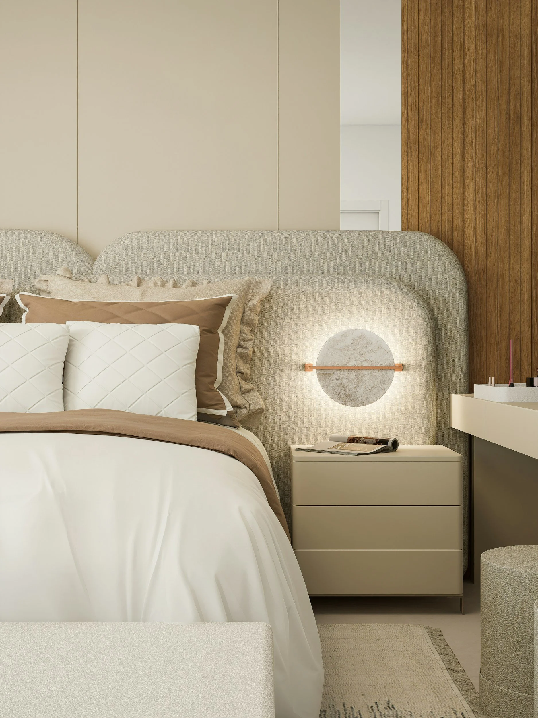 A bedroom with a beige upholstered bed, white and beige bedding, a white nightstand with a magazine and a distinctive circular wall-mounted light fixture, a wooden-paneled wall, and minimal decor.