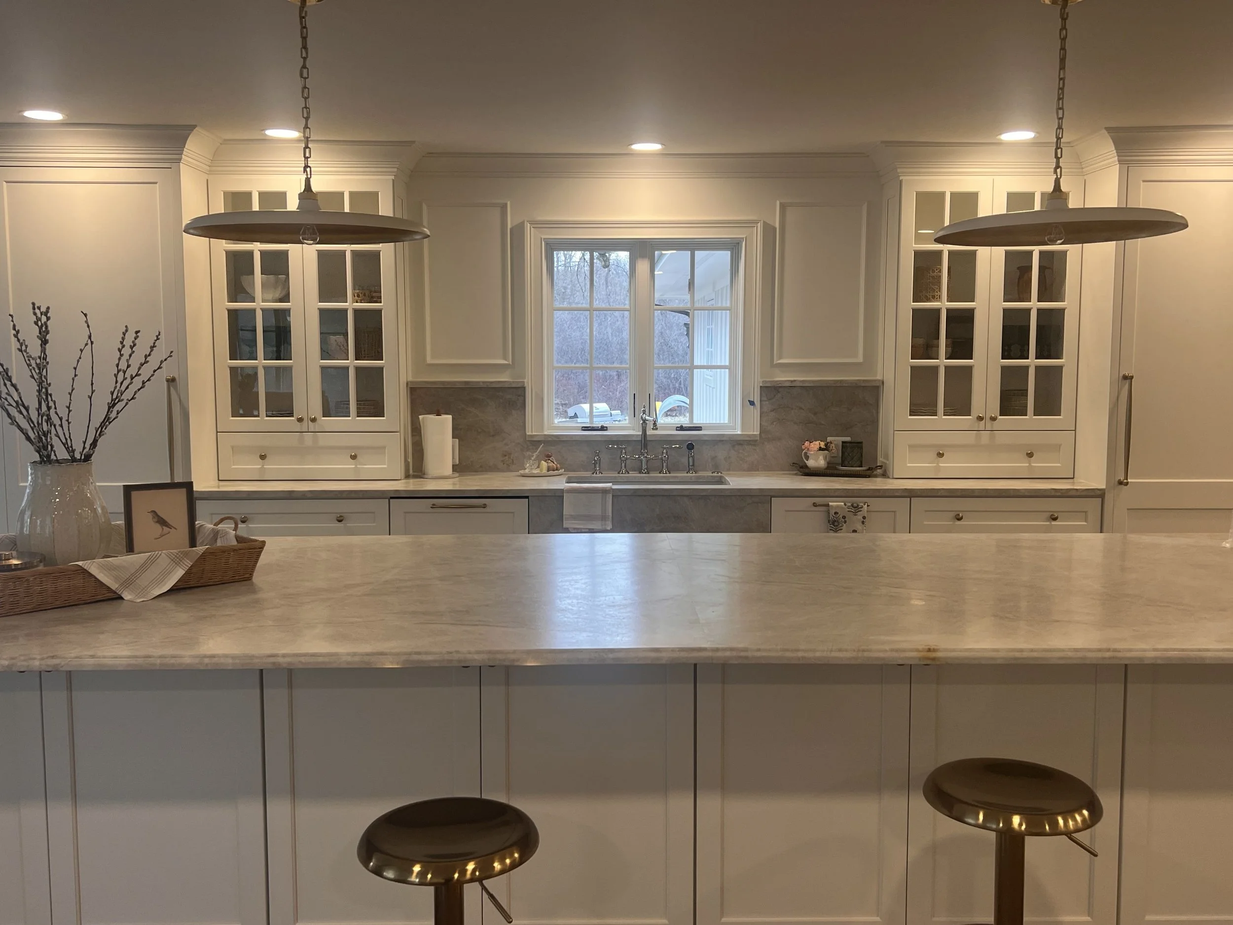Kitchen with white cabinets, a window above the sink, two hanging pendant lights, and two brown bar stools at the counter.