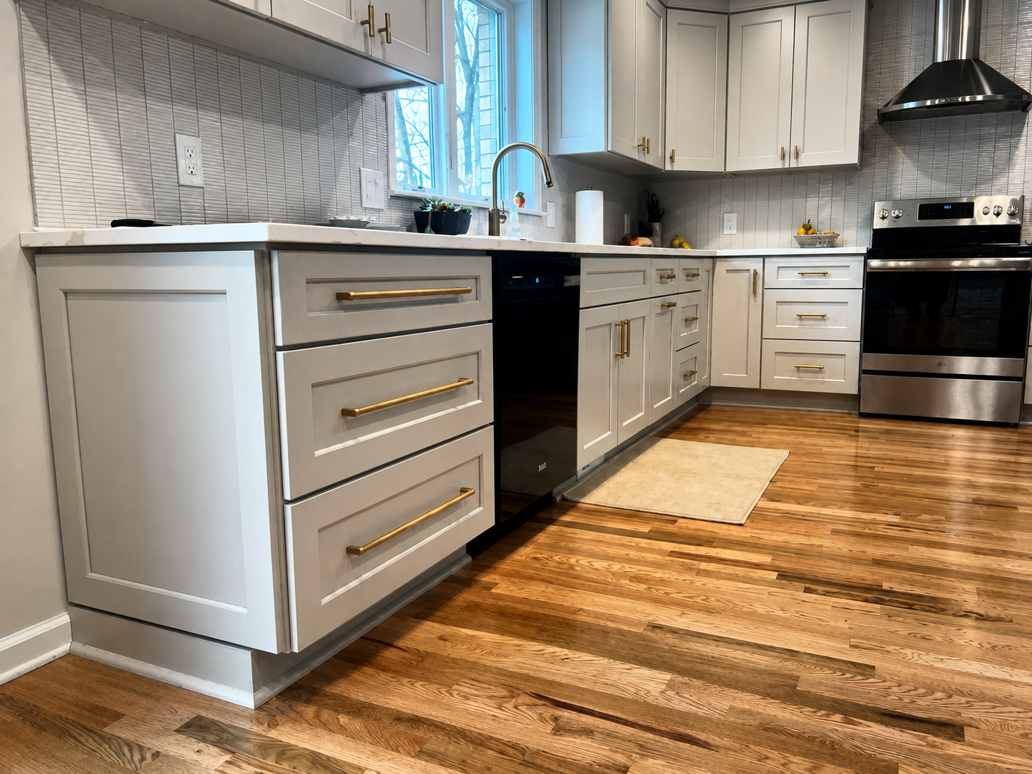 Modern Oakland County kitchen with white cabinetry, gold handles, hardwood floors, and stainless steel appliances.