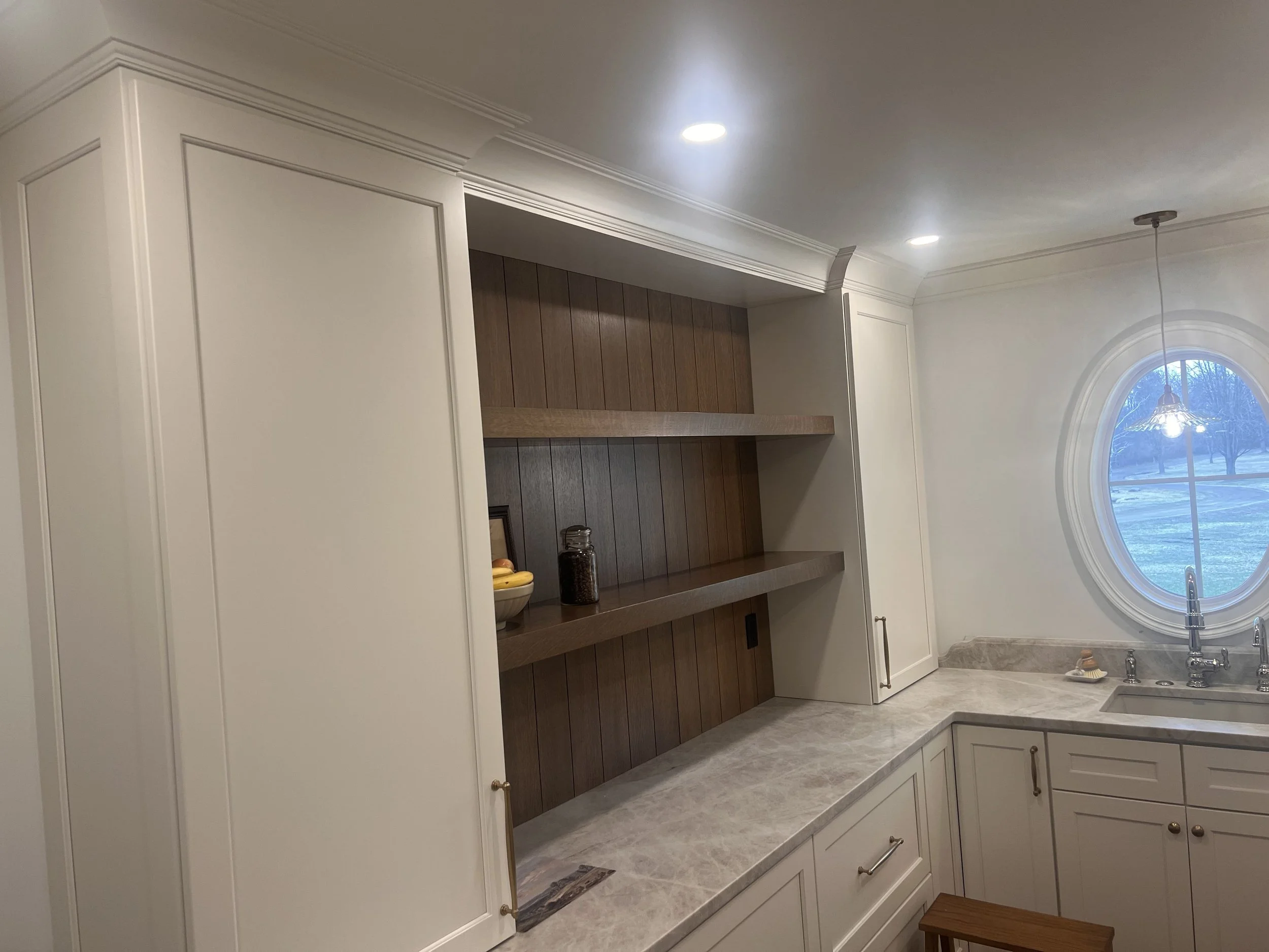 Kitchen with white cabinets, a marble countertop, a window with an arched top, and recessed ceiling lights. There is a fruit bowl and a glass jar on the shelf.