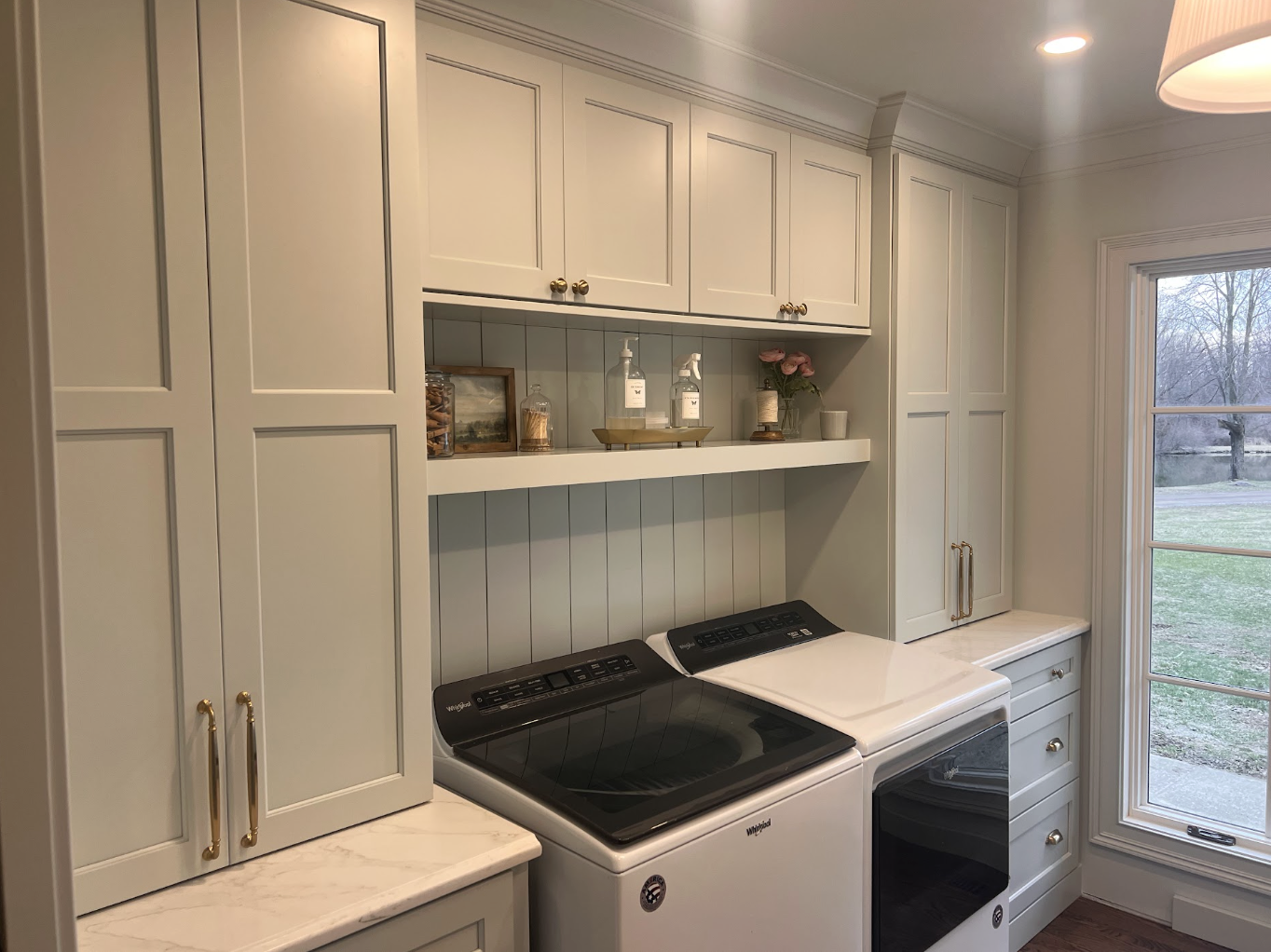 Laundry room with white cabinets, a Whirlpool washer and dryer, and a window showing a yard outside.