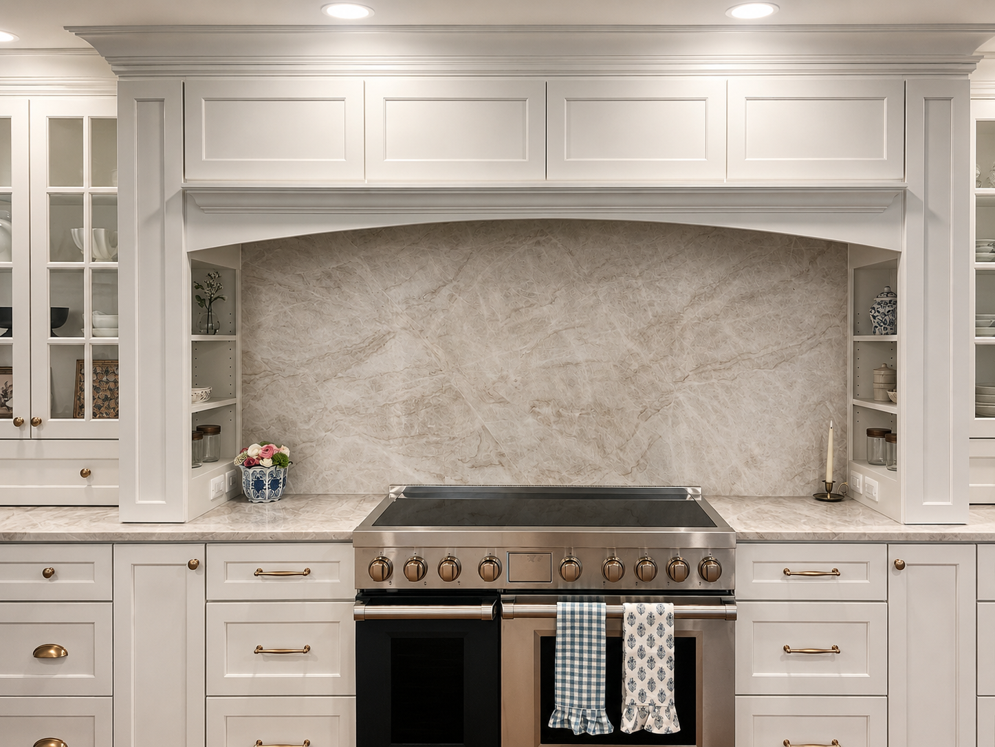 A modern kitchen with white cabinetry, a marble backsplash, and a stainless steel stove. The kitchen has open shelves with dishes and decorative items, a potted plant, a candle, and towels hanging from the stove handle.
