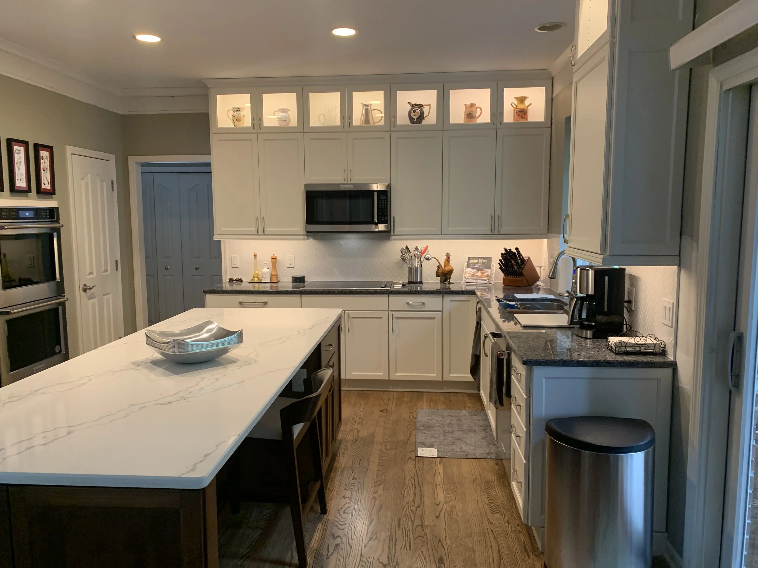 A modern kitchen with white cabinetry, black countertops, a microwave oven, and a marble kitchen island with bowls and seating.